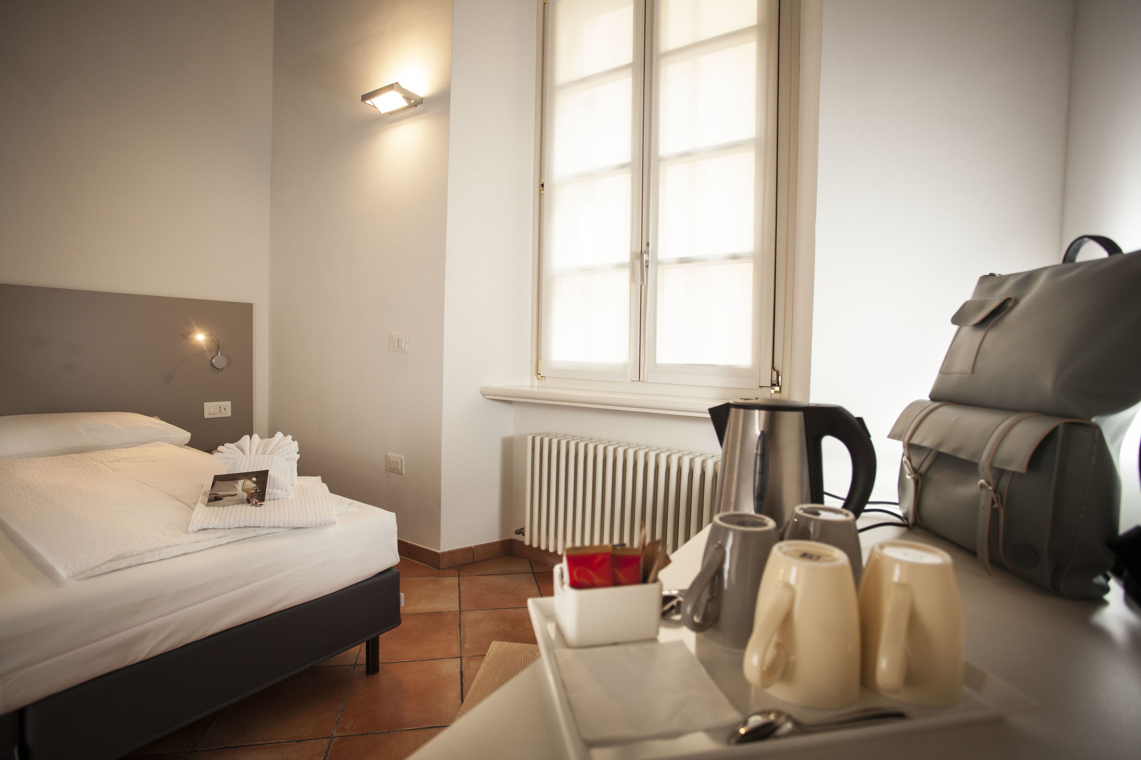 Una habitación de hotel con cama, radiador, ventana y una mesa con tetera y tazas.