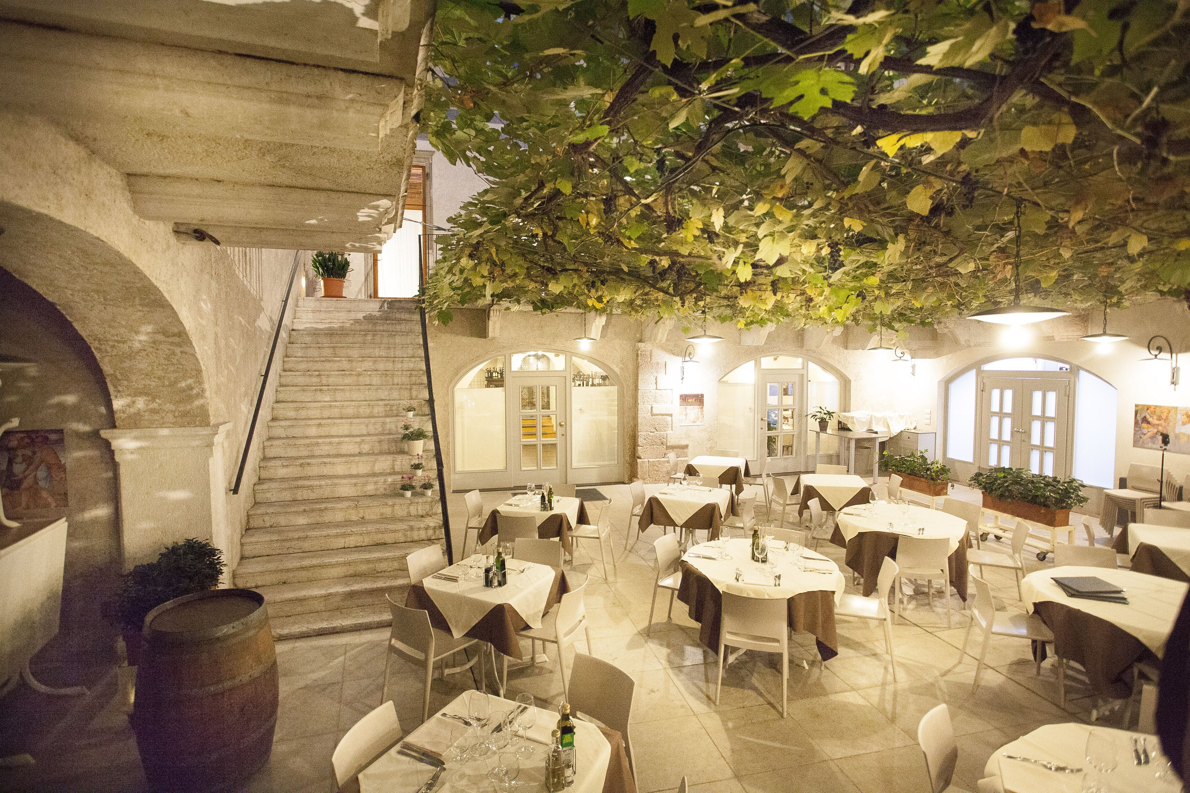 An indoor dining area with tables and chairs, a staircase, and potted plants.