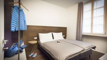 A modern hotel room with a large bed, a wooden headboard, a small round table, and a window with curtains.