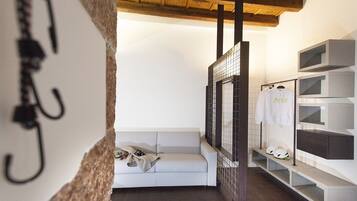 Ein modernes Badezimmer mit Waschbecken, Spiegel und Handtuchhalter. Im Hintergrund steht ein weißes Sofa und ein Regal mit Schuhen und einem Helm.