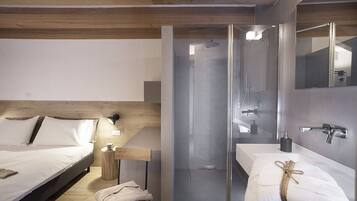 Una habitación de hotel moderna con cama, mesita de noche, lámpara y zona de ducha con paredes de vidrio.