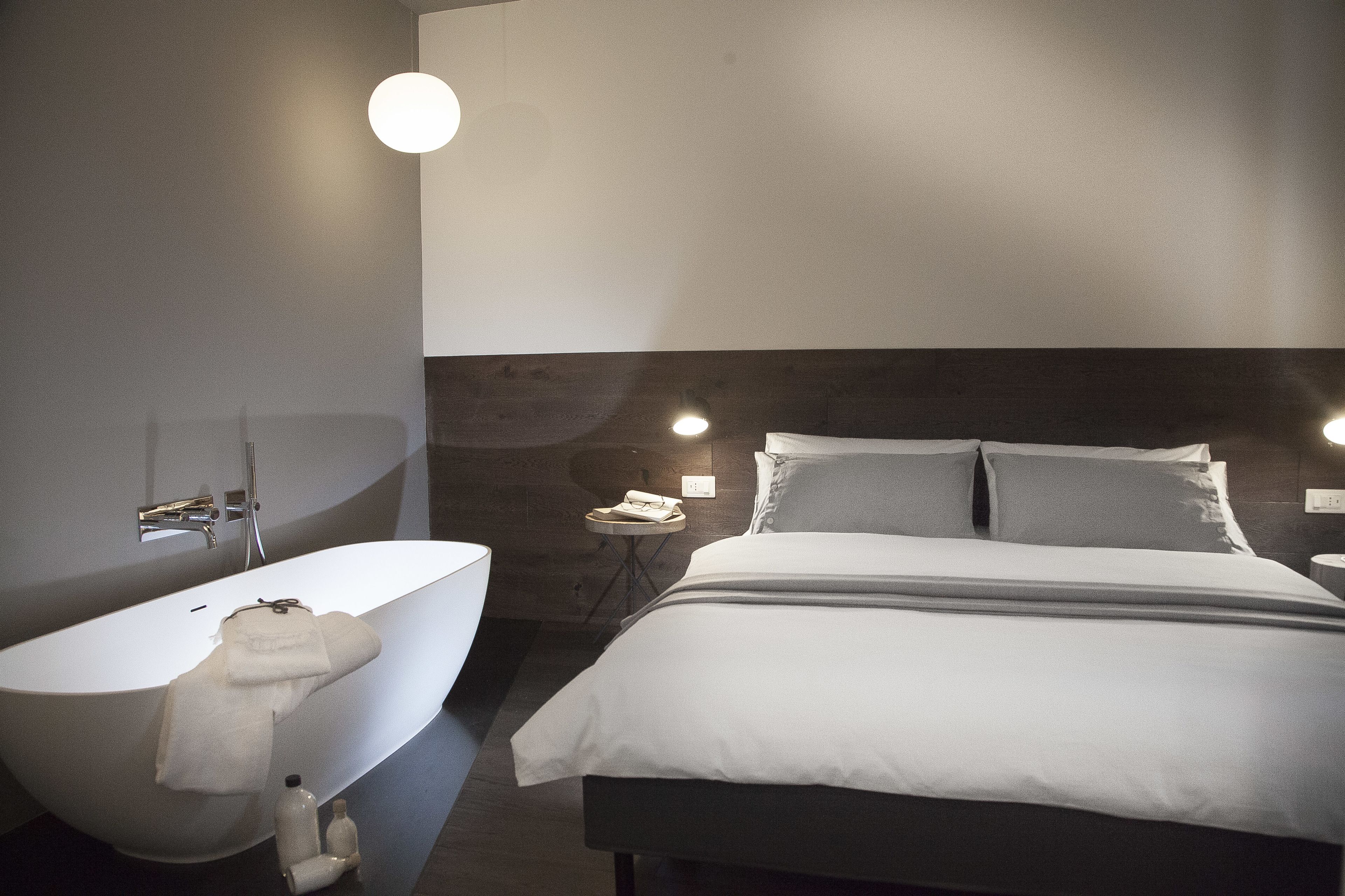 A modern bathroom with a freestanding bathtub, a toilet, and a bedside table with a lamp.