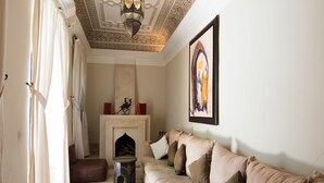 A living room with a beige sofa, a fireplace, and a painting on the wall. - Riad El Gnaouia (Marrakech)