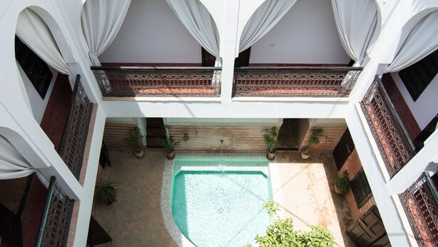A courtyard with a central pool, white walls, and arched balconies with draped curtains. - Riad El Gnaouia (Marrakech)