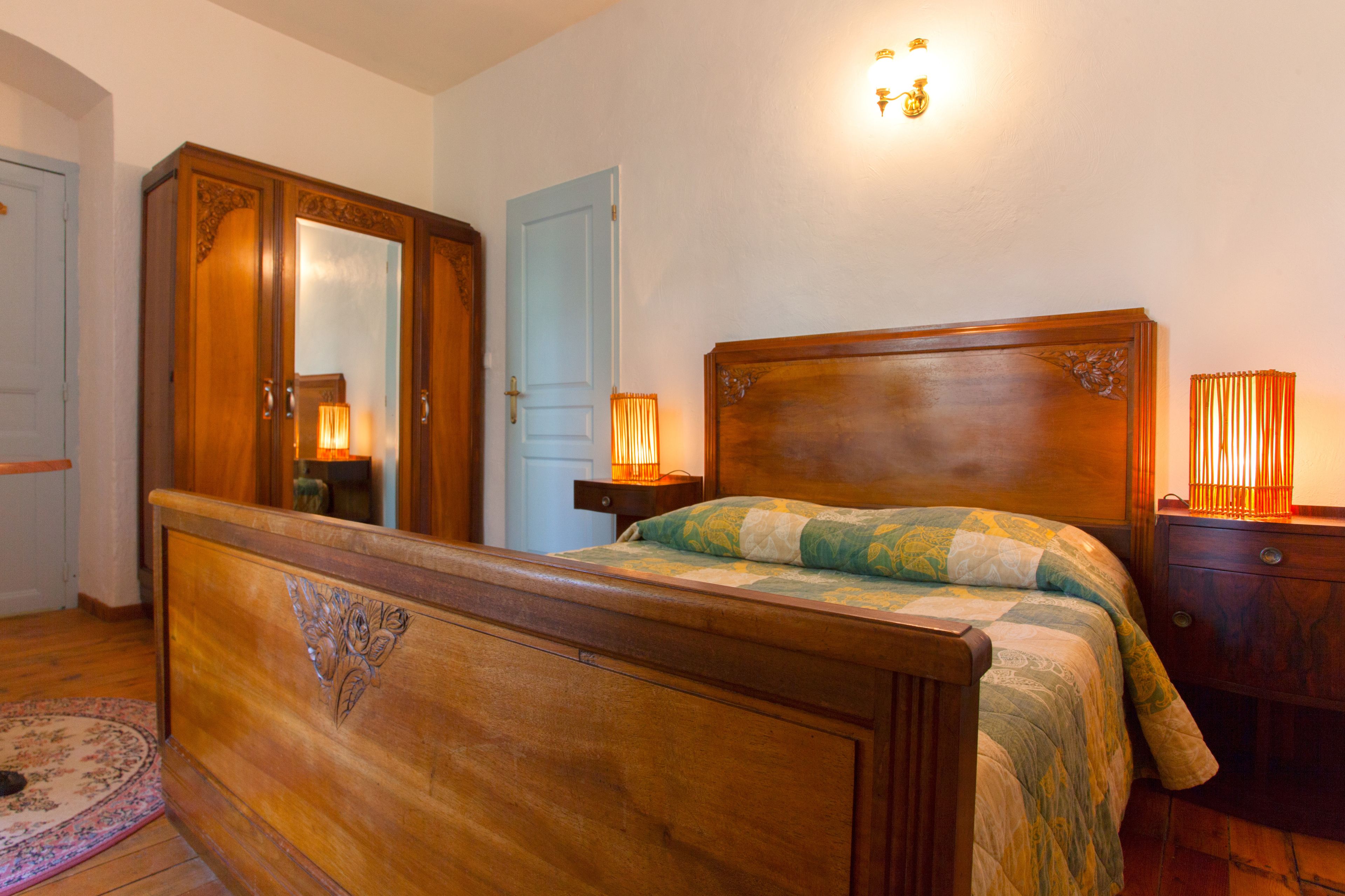 Une chambre à coucher avec un lit en bois, une table de chevet, une commode, un miroir et un luminaire fixé au mur.