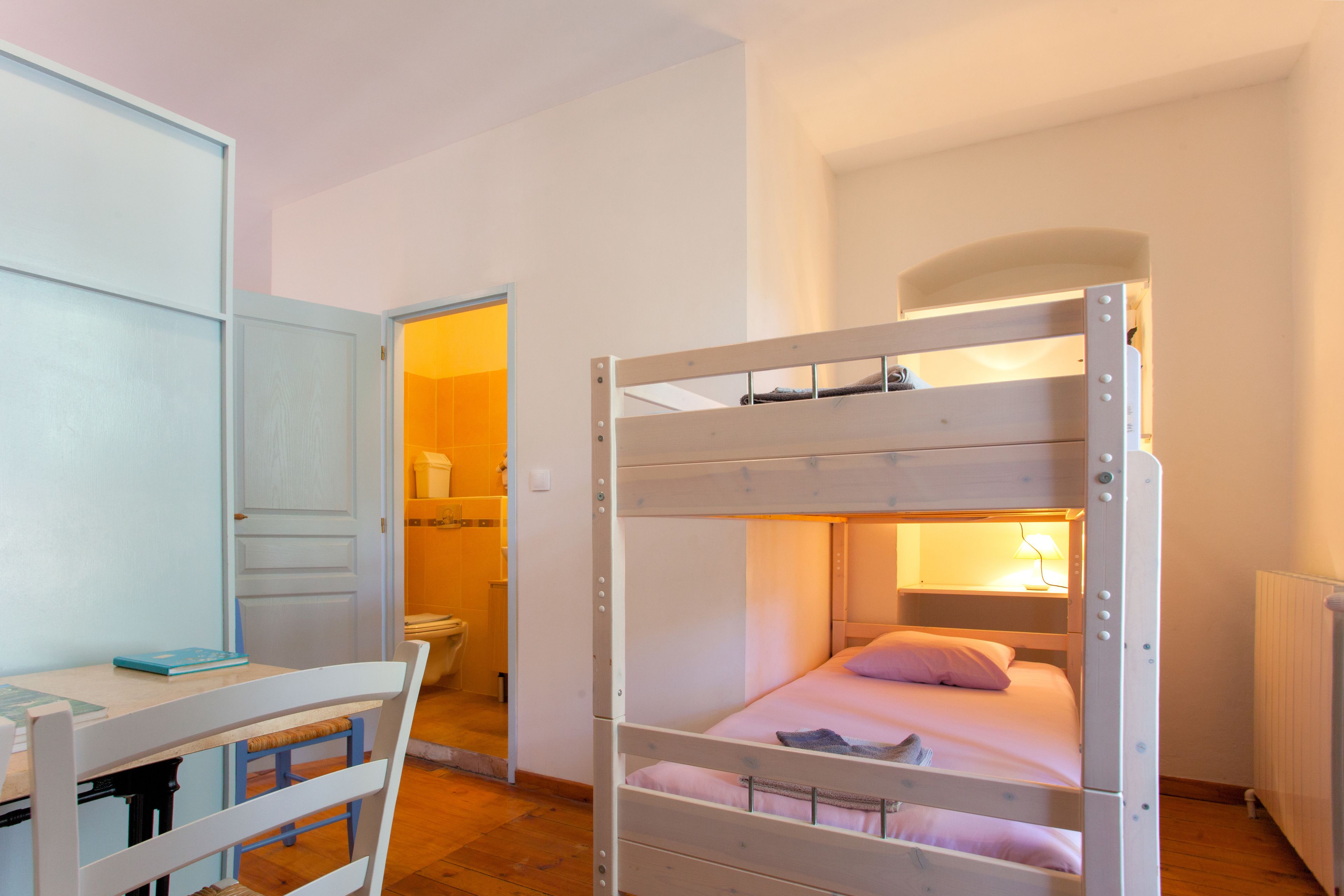 A bunk bed with a desk and chair, a bathroom with a toilet and sink, and a radiator.