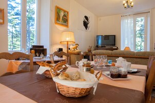 Uma área de refeições com uma mesa posta para o café da manhã, incluindo pão, doces e acompanhamentos.