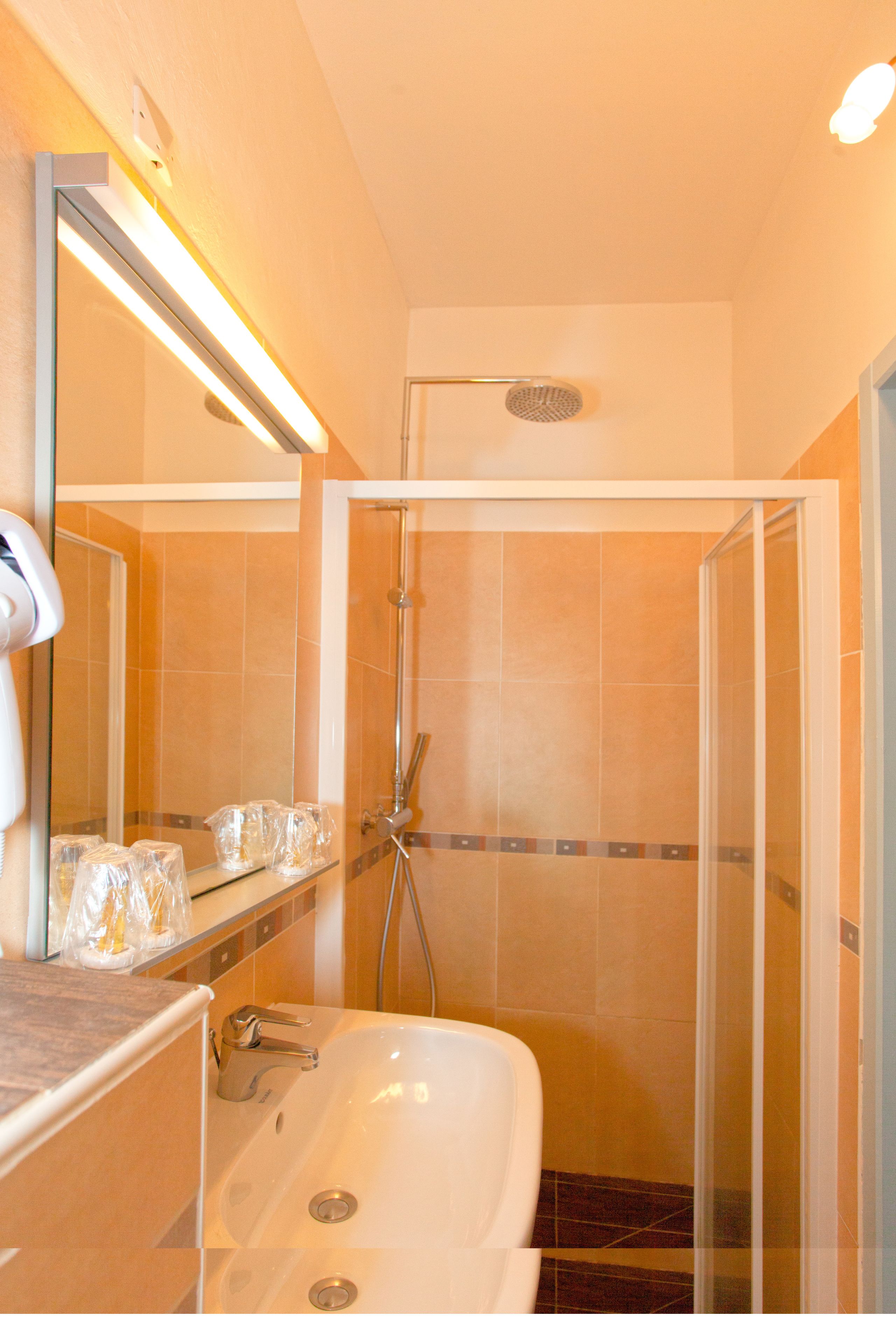 Ein Badezimmer mit einer gläsernen Duschkabine, einer weißen Badewanne und einem Waschtisch mit Spiegel und Pflegeprodukten.