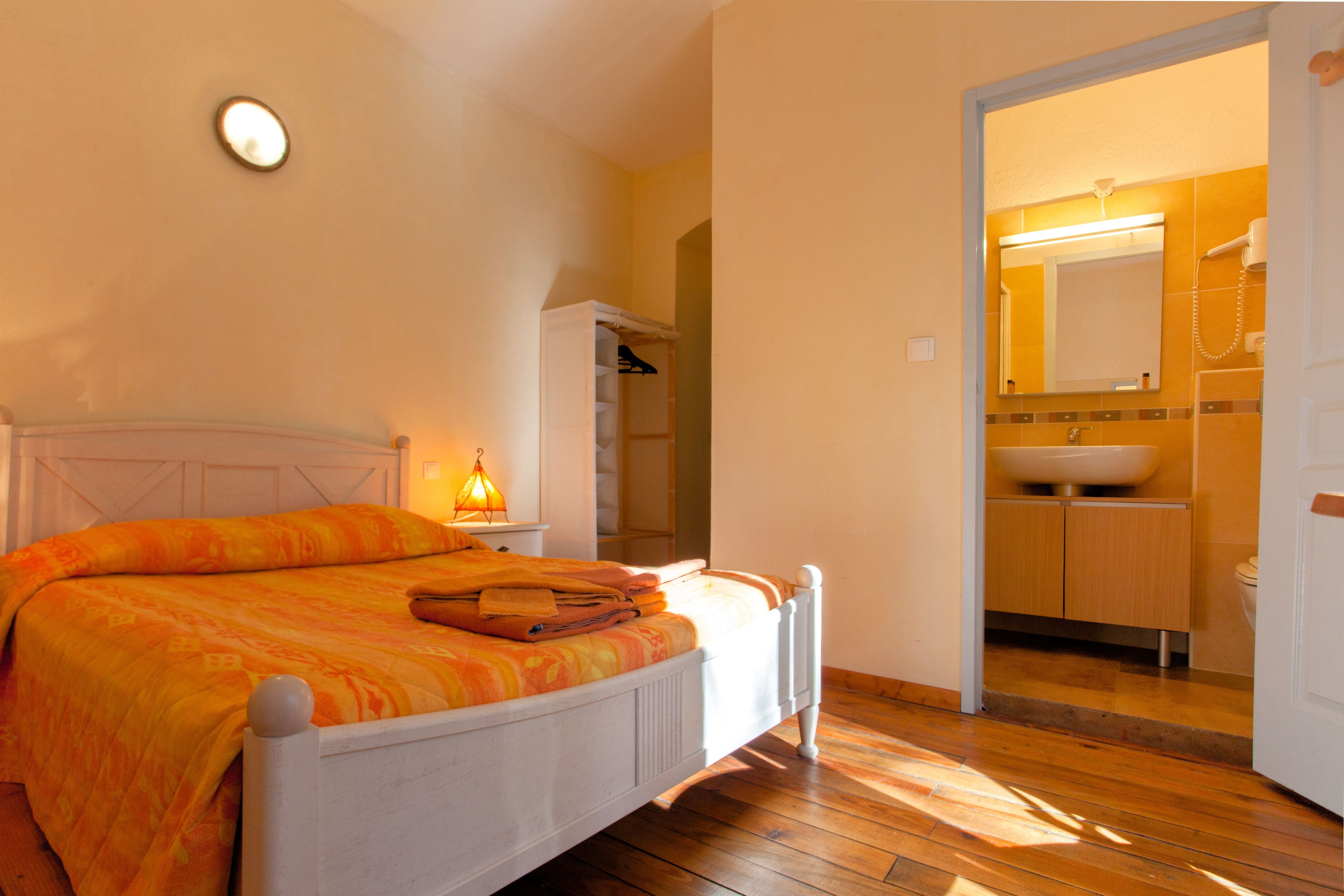 Quarto com cama, mesa de cabeceira com luminária, armário e banheiro com pia e espelho.