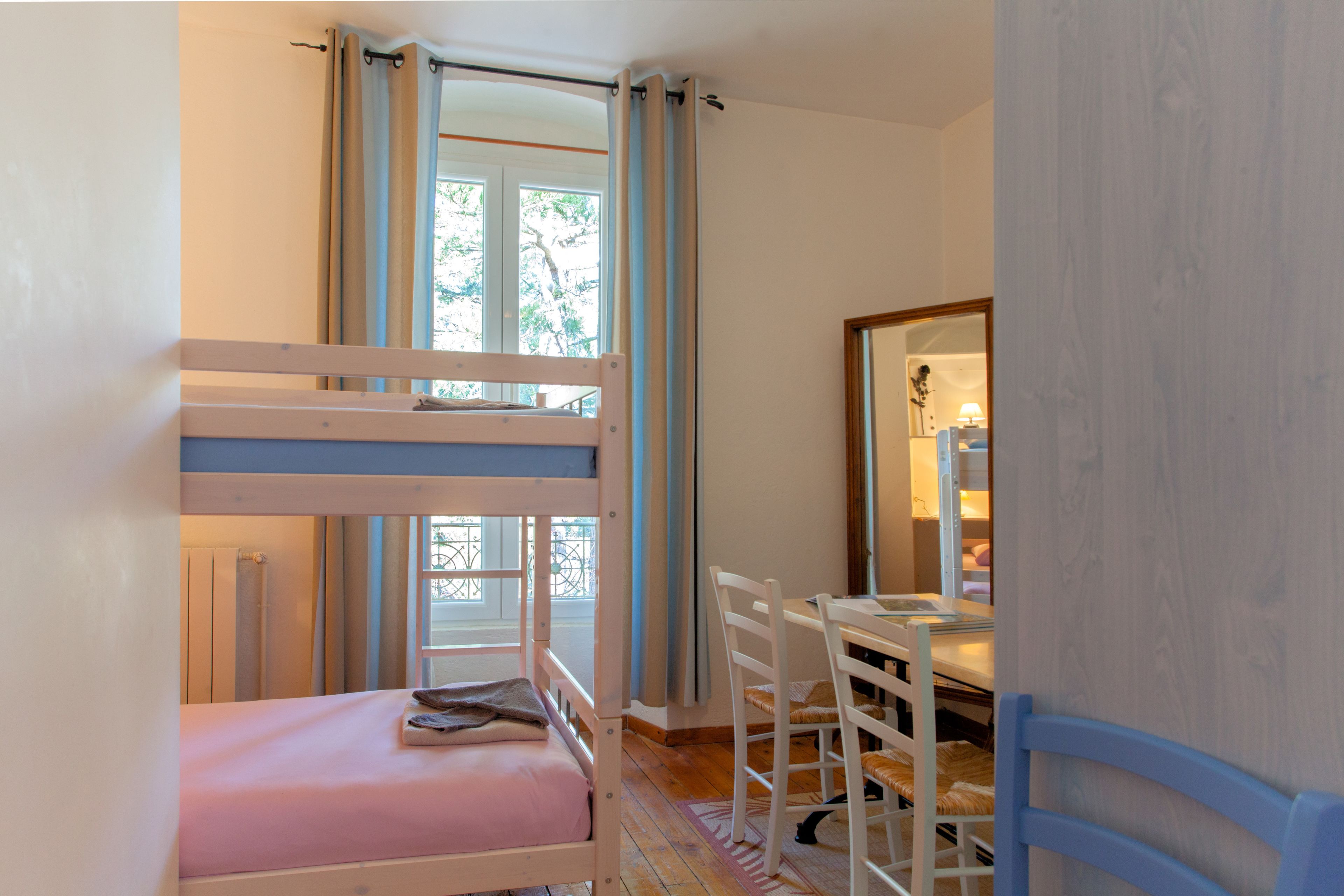 Un lit superposé avec un matelas rose, un bureau en bois avec une chaise et une fenêtre avec des rideaux.