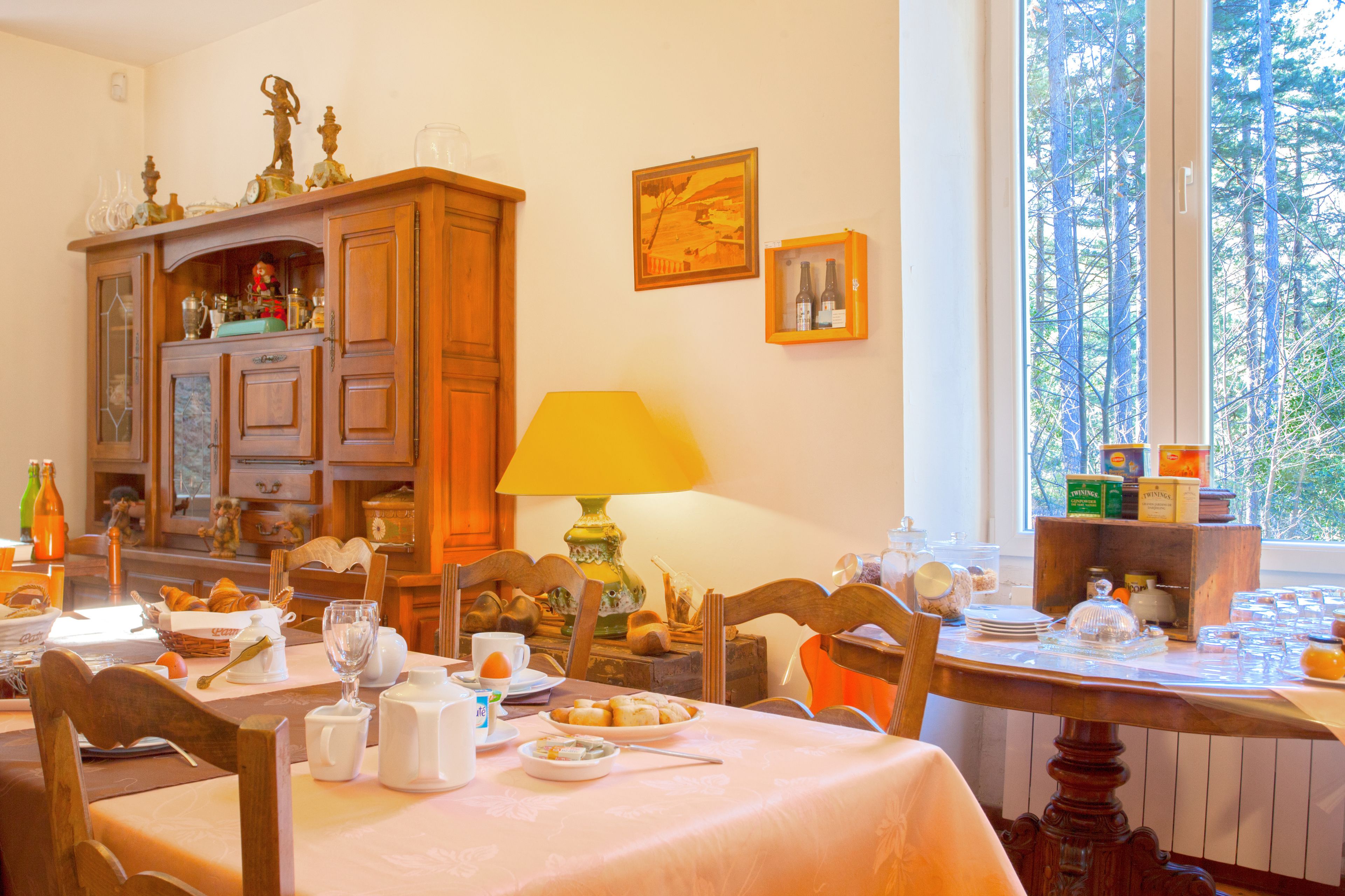 A dining area with a table set for breakfast, wooden furniture, and a window with a view of trees.