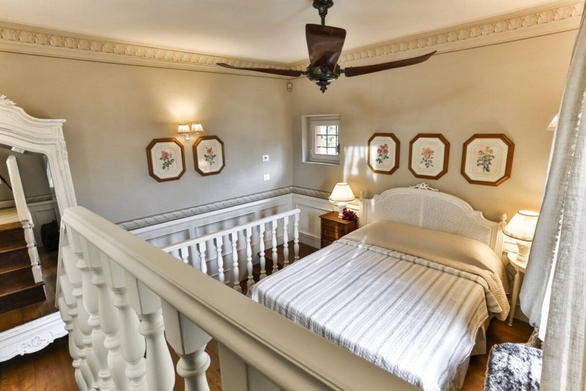Un dormitorio con una cama grande, un ventilador de techo, una mesita de noche, una lámpara y cuadros en la pared.