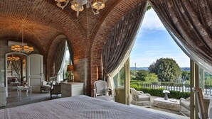 Un dormitorio espacioso con una cama grande, un rincón de descanso con sillones y vistas al exterior.