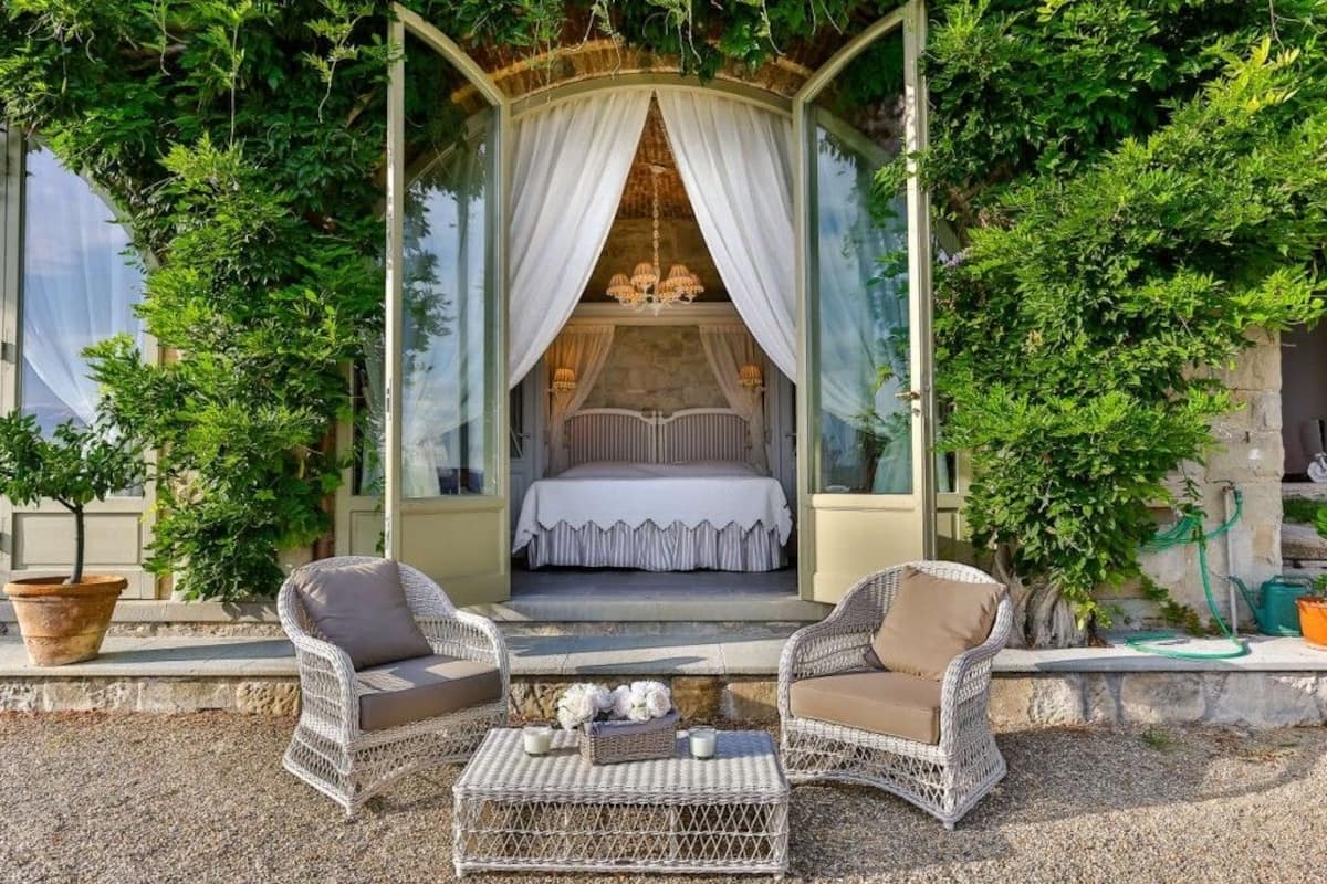 Un rincón acogedor al aire libre con mobiliario de mimbre y vistas a un dormitorio con cama a dosel.