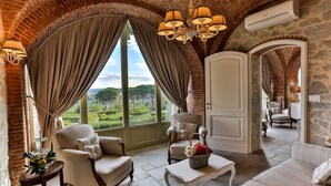 Una habitación amplia con un techo abovedado de ladrillo, grandes ventanales que ofrecen vistas a zonas verdes, y un candelabro.