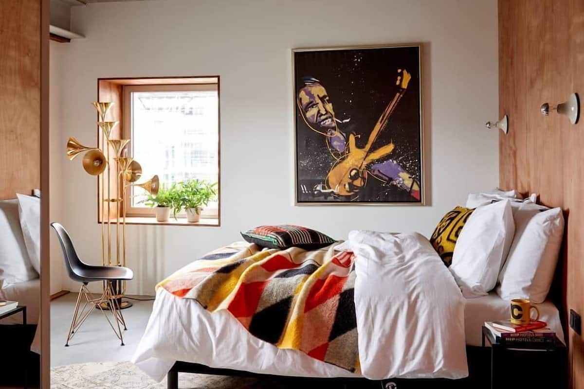 A modern bedroom with a bed, a desk, and a window with plants.