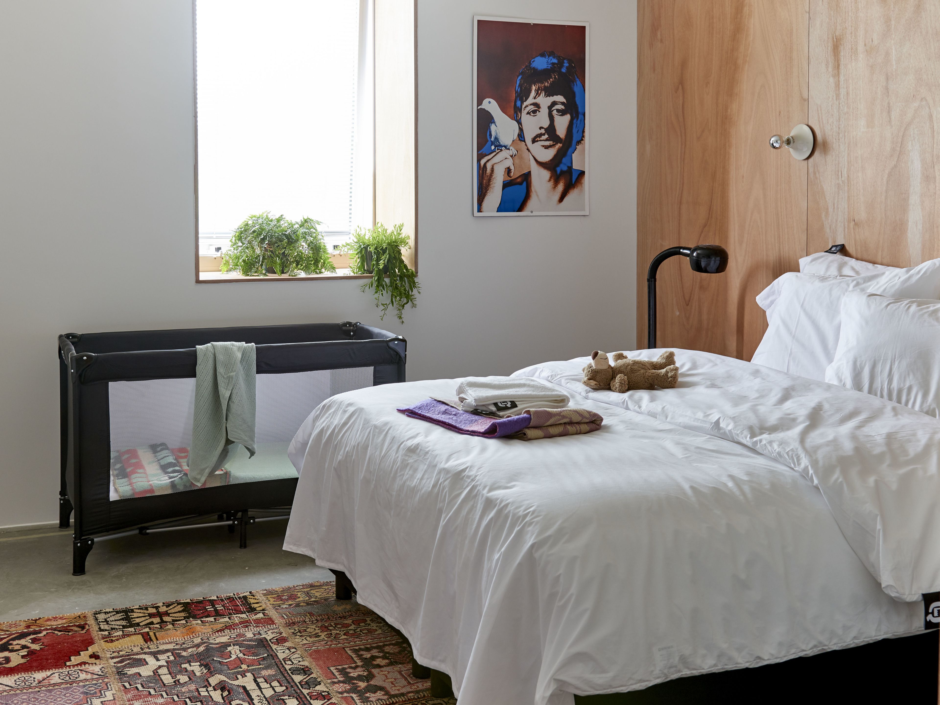 Een slaapkamer met een bed, een kinderbedje, een raam met uitzicht, een plant en een poster aan de muur.