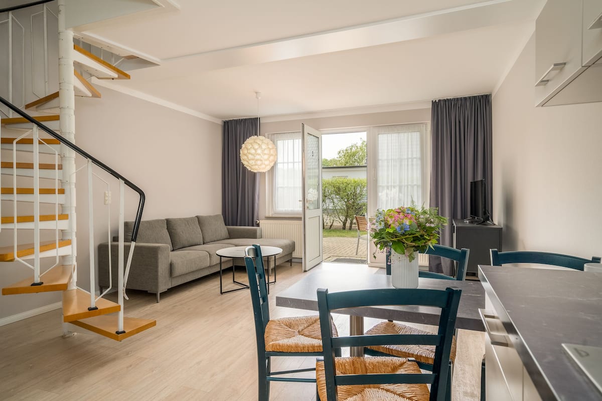 Una sala de estar moderna con una escalera, un comedor y vistas al exterior.
