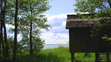 A rustic wooden structure with a thatched roof, surrounded by lush greenery and overlooking a body of water.