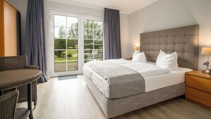 A hotel room with a large bed, a wooden nightstand, a wicker chair, and a sliding glass door leading to a balcony. - Hotel Müritz - Park (Rechlin)