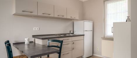 Una cocina compacta con una mesa y sillas, un refrigerador y una ventana con cortinas.