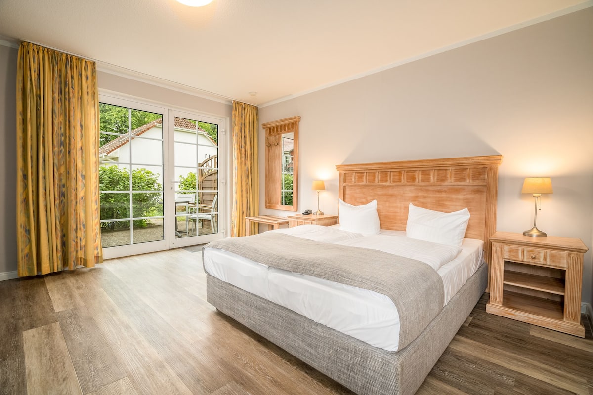 Un dormitorio con una cama grande, cabecera de madera, dos mesitas de noche con lámparas y una puerta corredera de vidrio que da a un balcón.