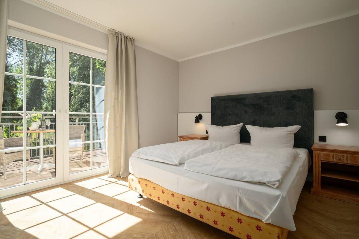Un dormitorio con una cama grande, una mesita de noche, una lámpara y vistas a un espacio exterior con mobiliario a través de una puerta corrediza de cristal.