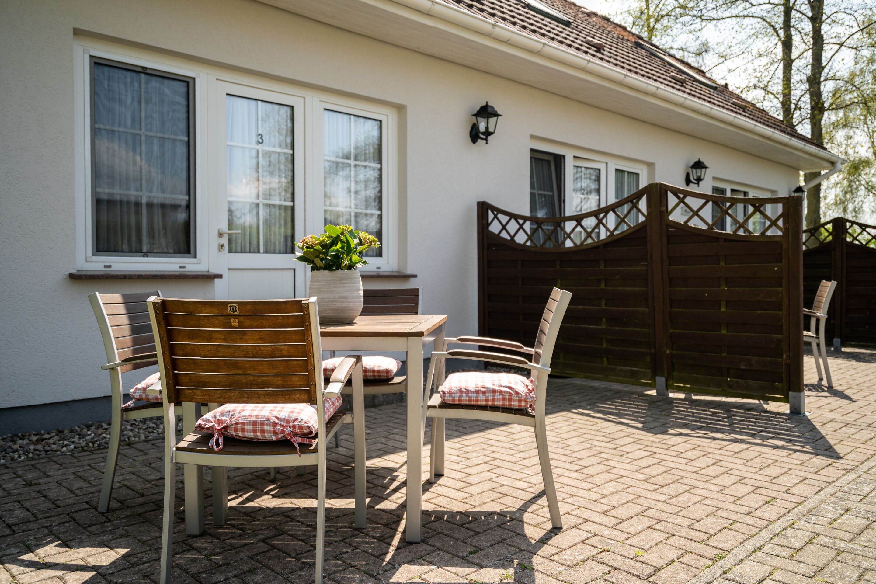 Une terrasse avec une table et des chaises, un pot de fleurs et un portail en bois.