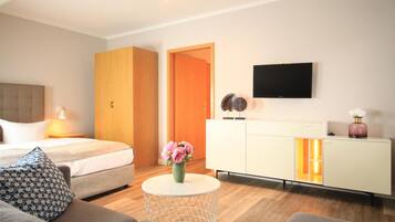 A modern hotel room with a bed, sofa, round coffee table, TV, and a cabinet with a glass door.