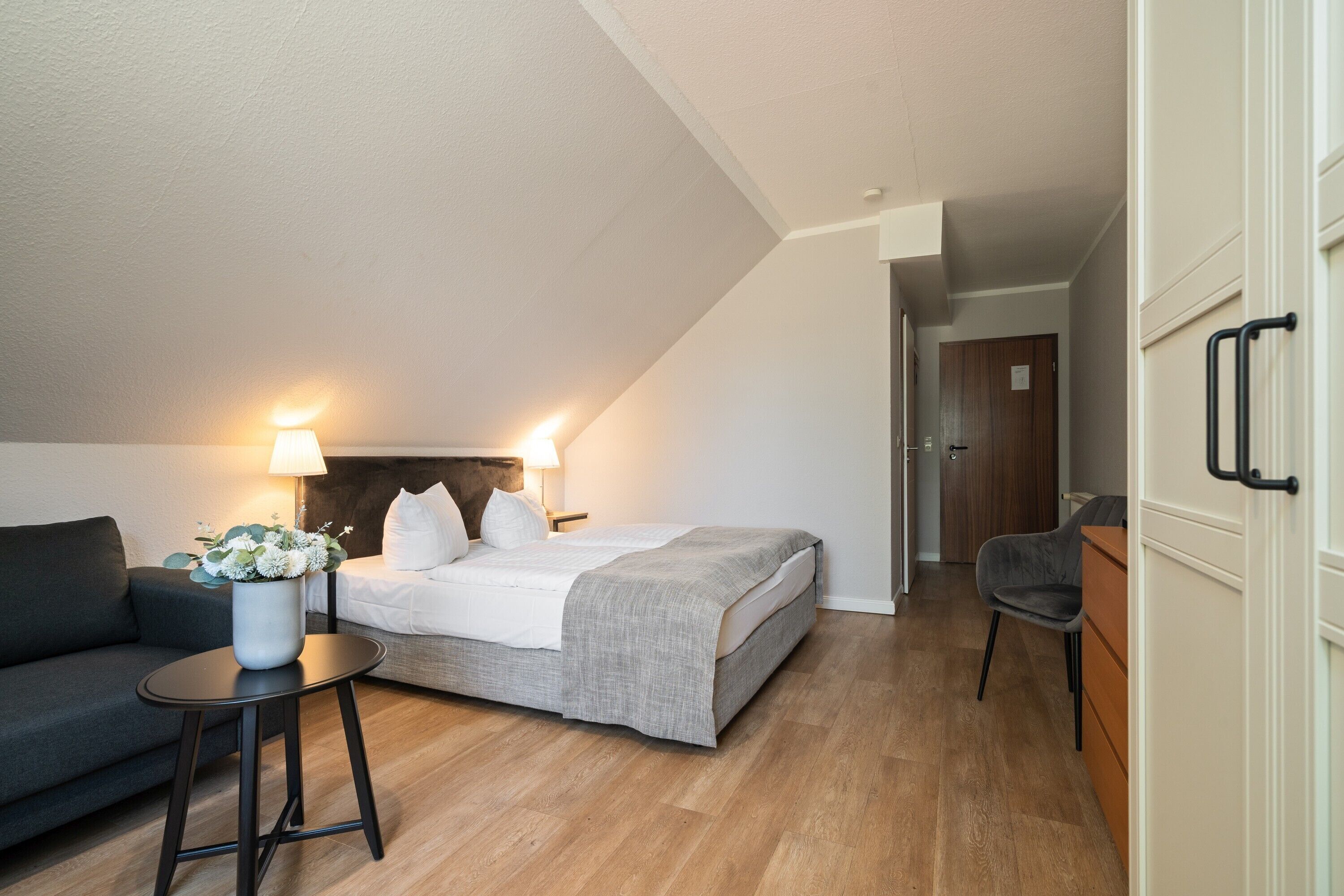 A modern bedroom with a bed, bedside table, lamp, and a small table with a vase.