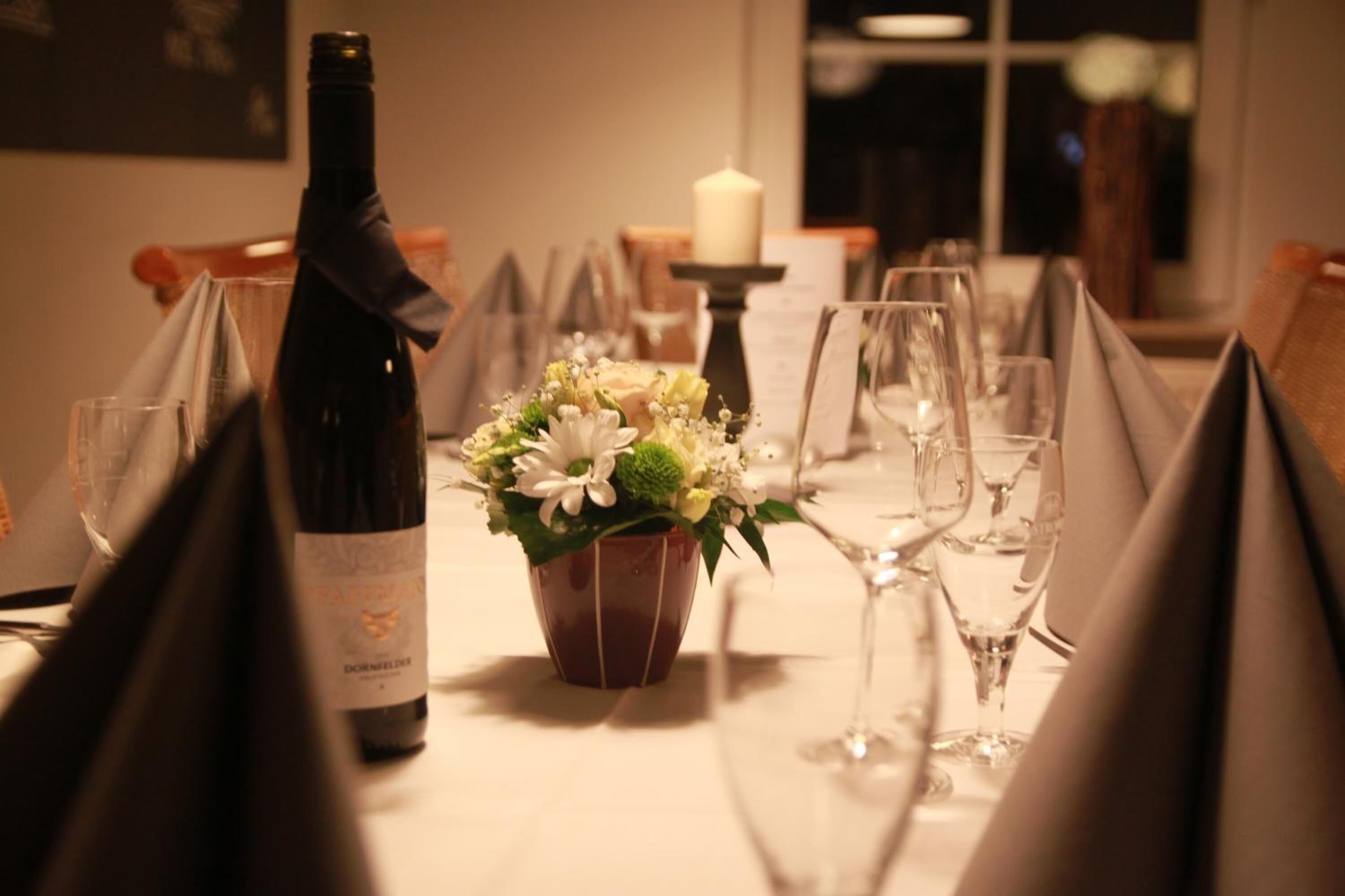 Una mesa de comedor con copas de vino, una botella de vino y un centro de mesa floral.