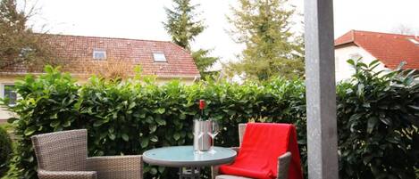 Une terrasse extérieure avec des meubles en osier, une table et une bouteille de vin.