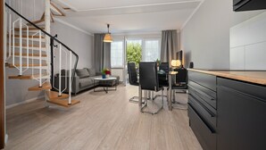 A modern living space with a staircase, a dining area, a sofa, and a kitchen. - Hotel Müritz - Park (Rechlin)