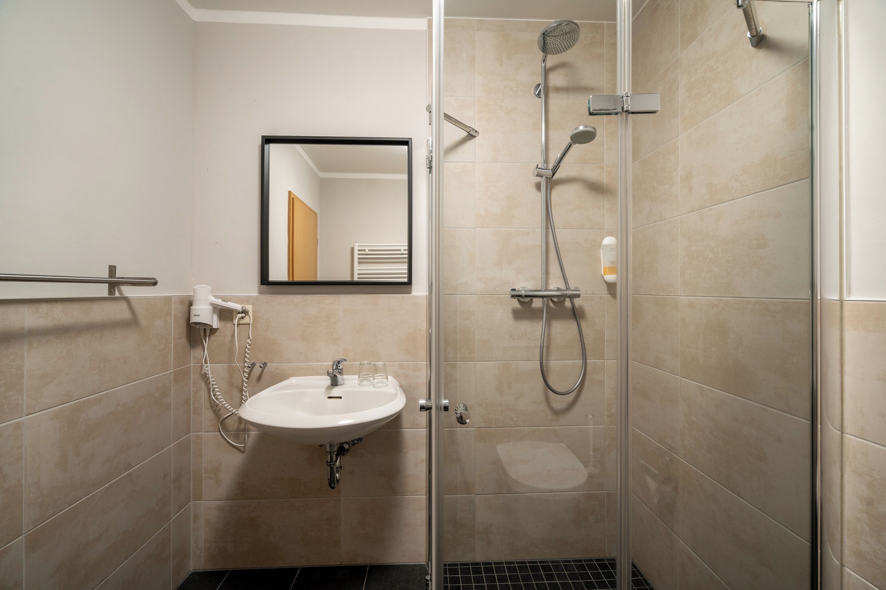 A modern bathroom with a glass-enclosed shower, a sink with a mirror above it, and beige tiles.
