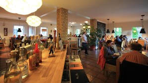A restaurant with a long wooden counter, various bottles, and books. There are people dining and a potted plant in the center. - Hotel Müritz - Park (Rechlin)