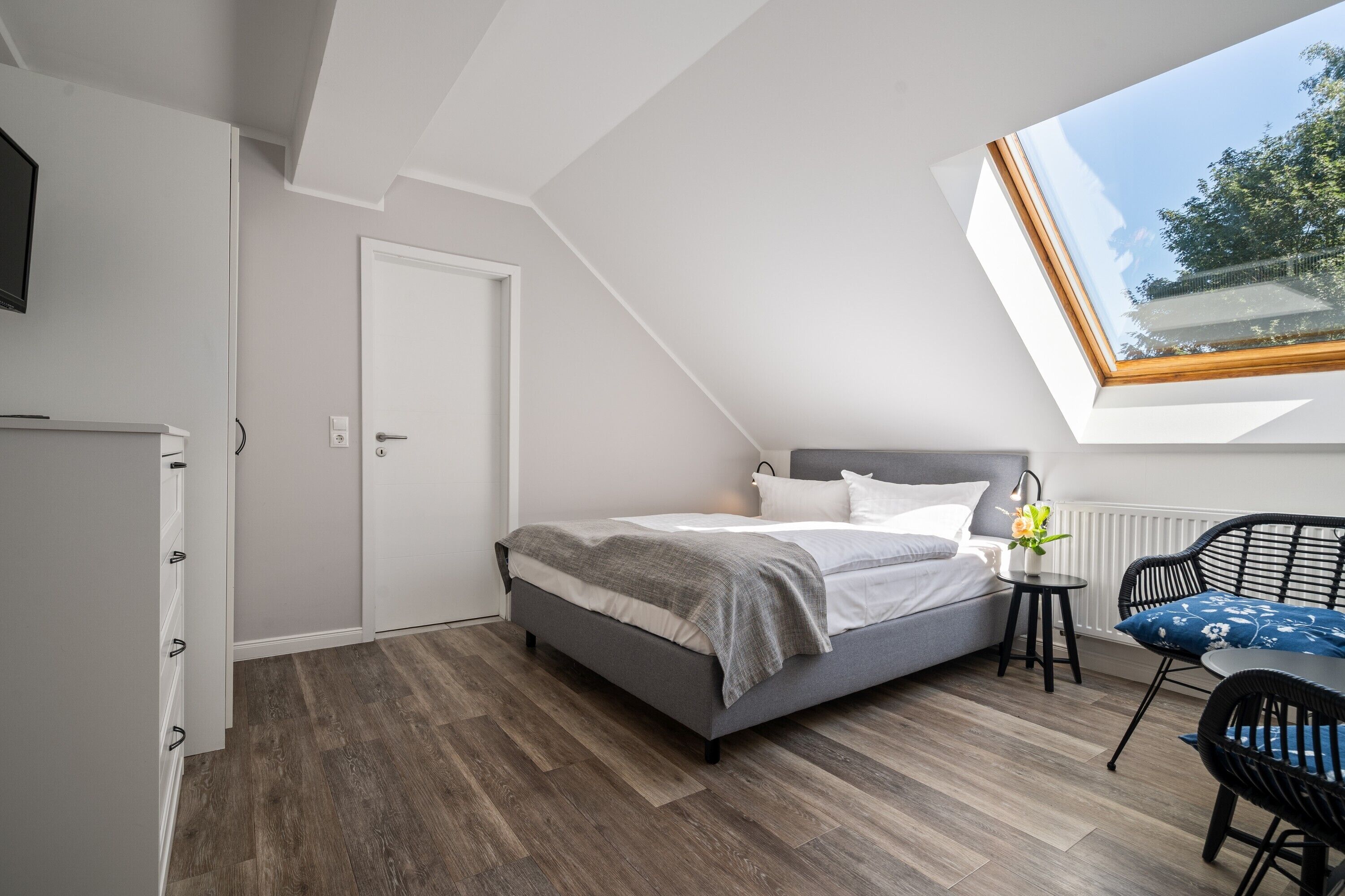 A bedroom with a skylight, a bed, a bedside table, a chair, and a wardrobe.