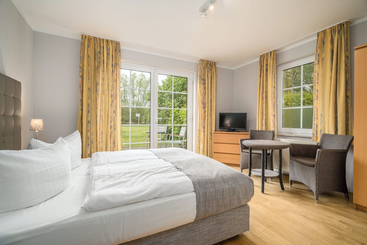 Habitación de hotel con una cama grande, televisión, escritorio con silla y ventanas amplias con cortinas.