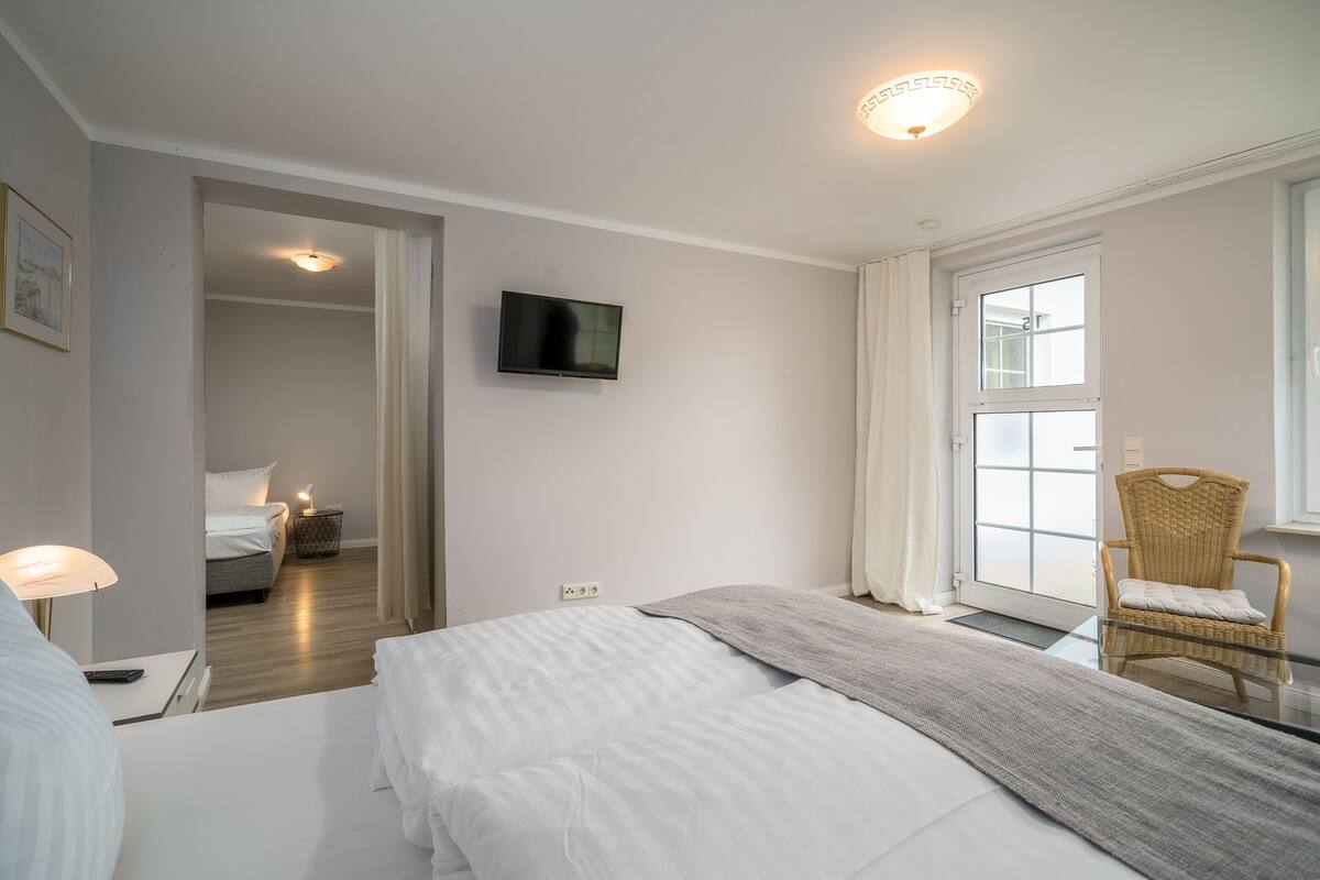 Una habitación de hotel con cama, mesita de noche, lámpara, televisor y una silla de mimbre.