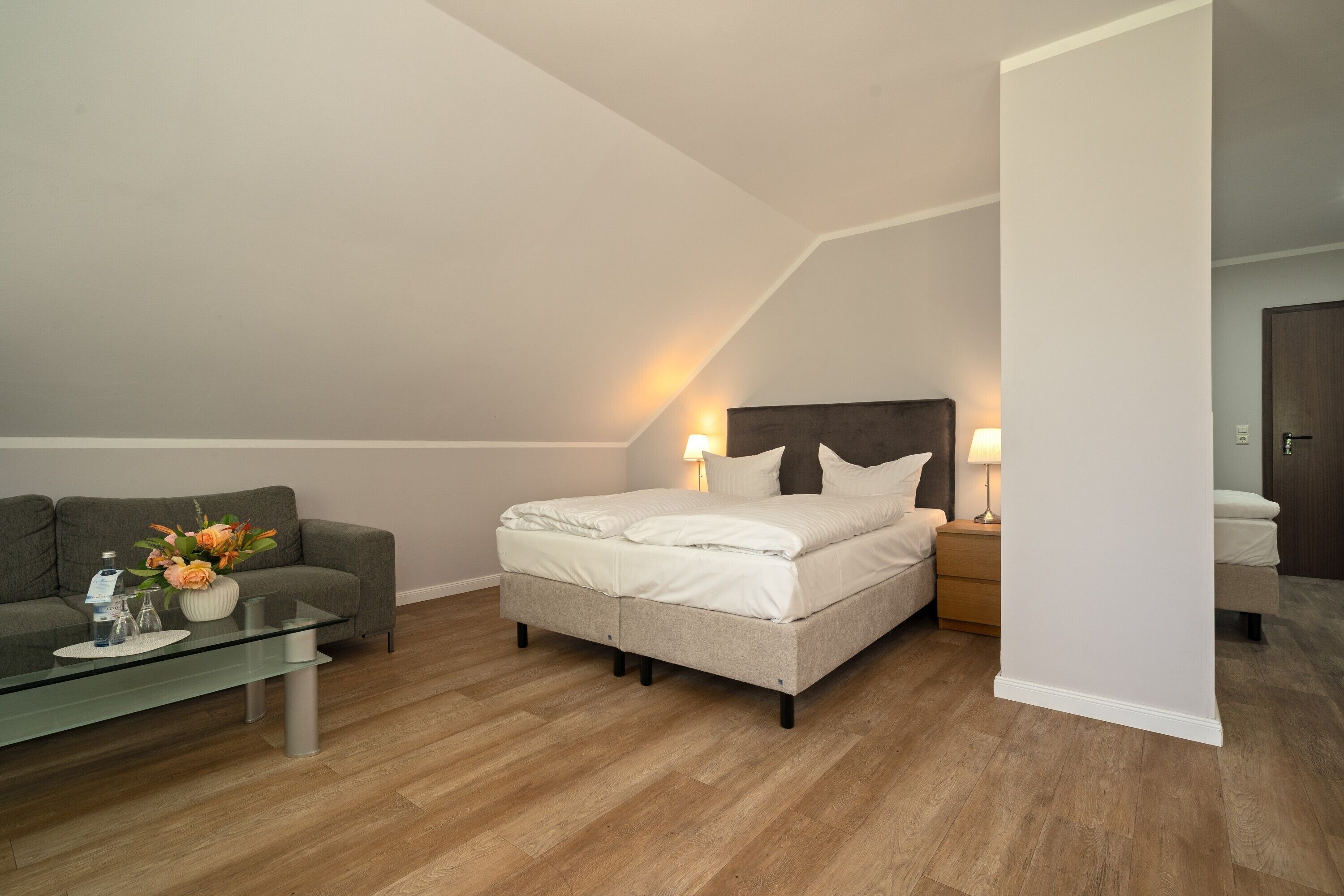 Un dormitorio con una cama, un sofá, una mesa de centro de vidrio y una mesita de noche con lámpara.