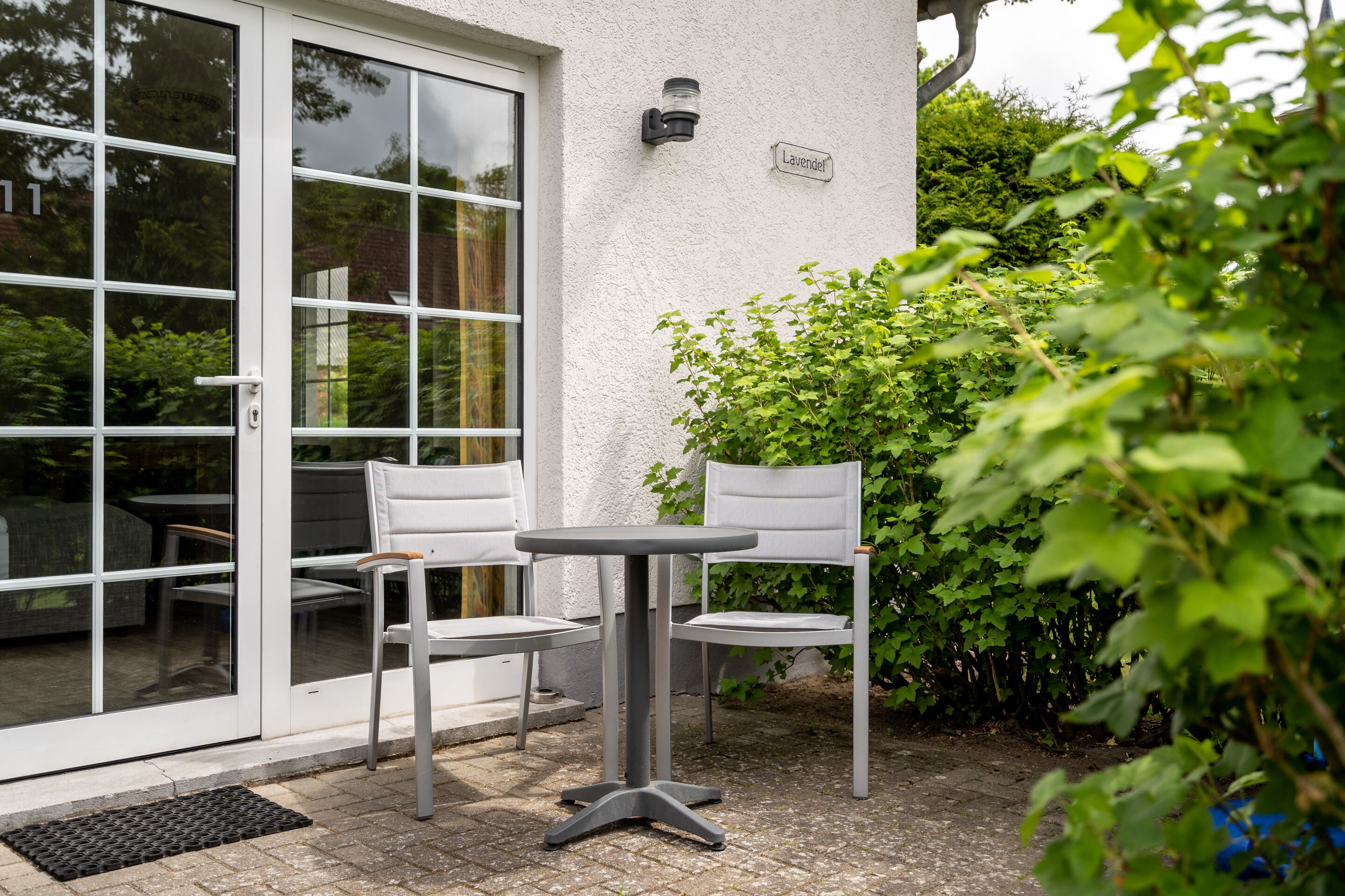 Une terrasse extérieure avec une table et deux chaises, une porte-fenêtre coulissante et une enseigne indiquant « Lavendel ».