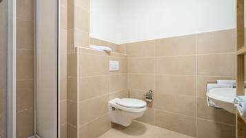 Ein Badezimmer mit beigen Fliesen, einer Toilette, einem Waschbecken und einem Handtuchhalter.
