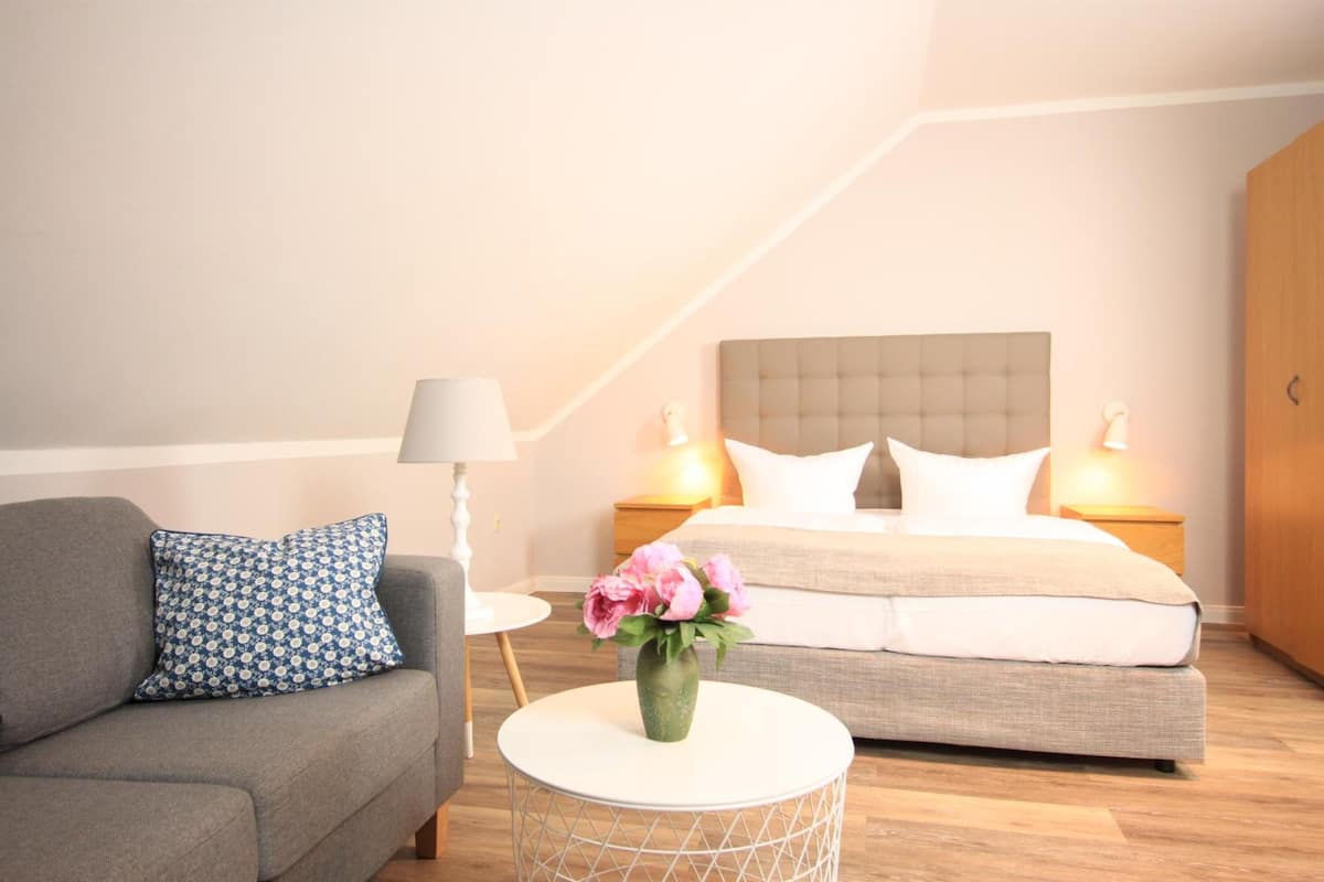 Un dormitorio moderno con una cama, un sofá, una mesita redonda y un florero con flores.