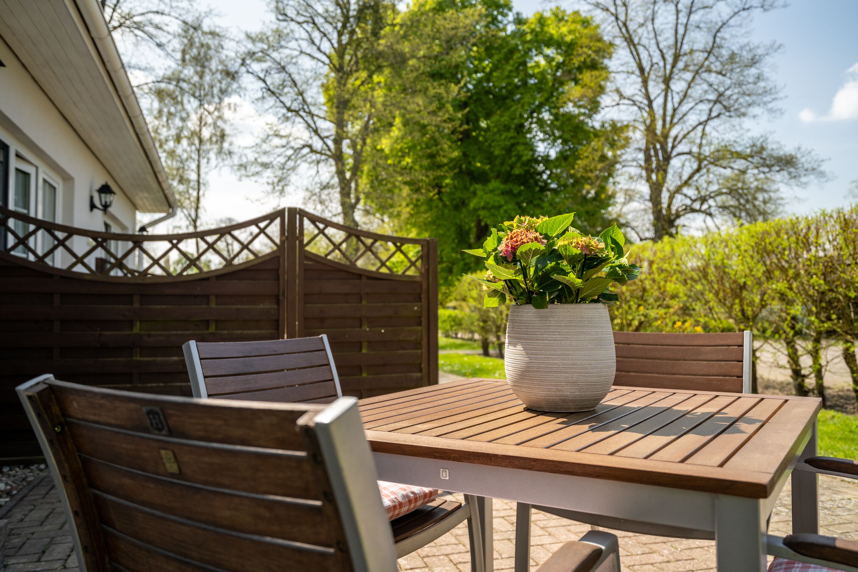 A wooden outdoor table with a potted plant, two chairs, and a wooden fence.