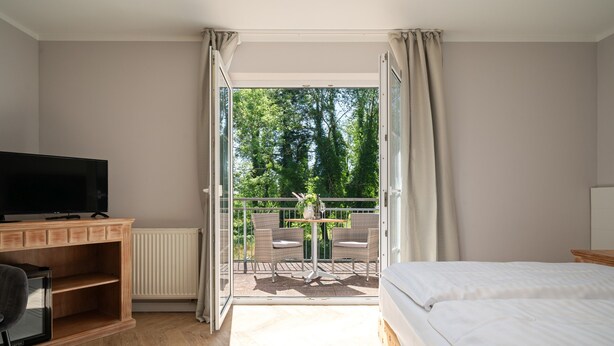 A bedroom with a bed, a TV, a desk, and a balcony with a table and chairs. - Hotel Müritz - Park (Rechlin)