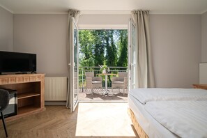 Un dormitorio con cama, televisión, escritorio y balcón con mesa y sillas.