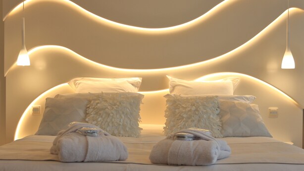 Ein modernes Schlafzimmer mit einem gewölbten Kopfteil, zwei Nachttischlampen und ordentlich gefalteten Handtüchern auf dem Bett.
