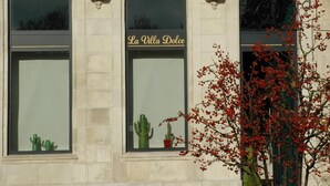 Eine Gebäudefassade mit drei Rundbogenfenstern, einem Balkon mit schmiedeeisernen Geländern und einem Schild mit der Aufschrift 'La Villa Dolce'.