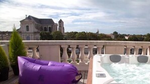 Eine Dachterrasse mit Whirlpool und einem violetten Liegestuhl mit Blick auf ein historisches Gebäude.