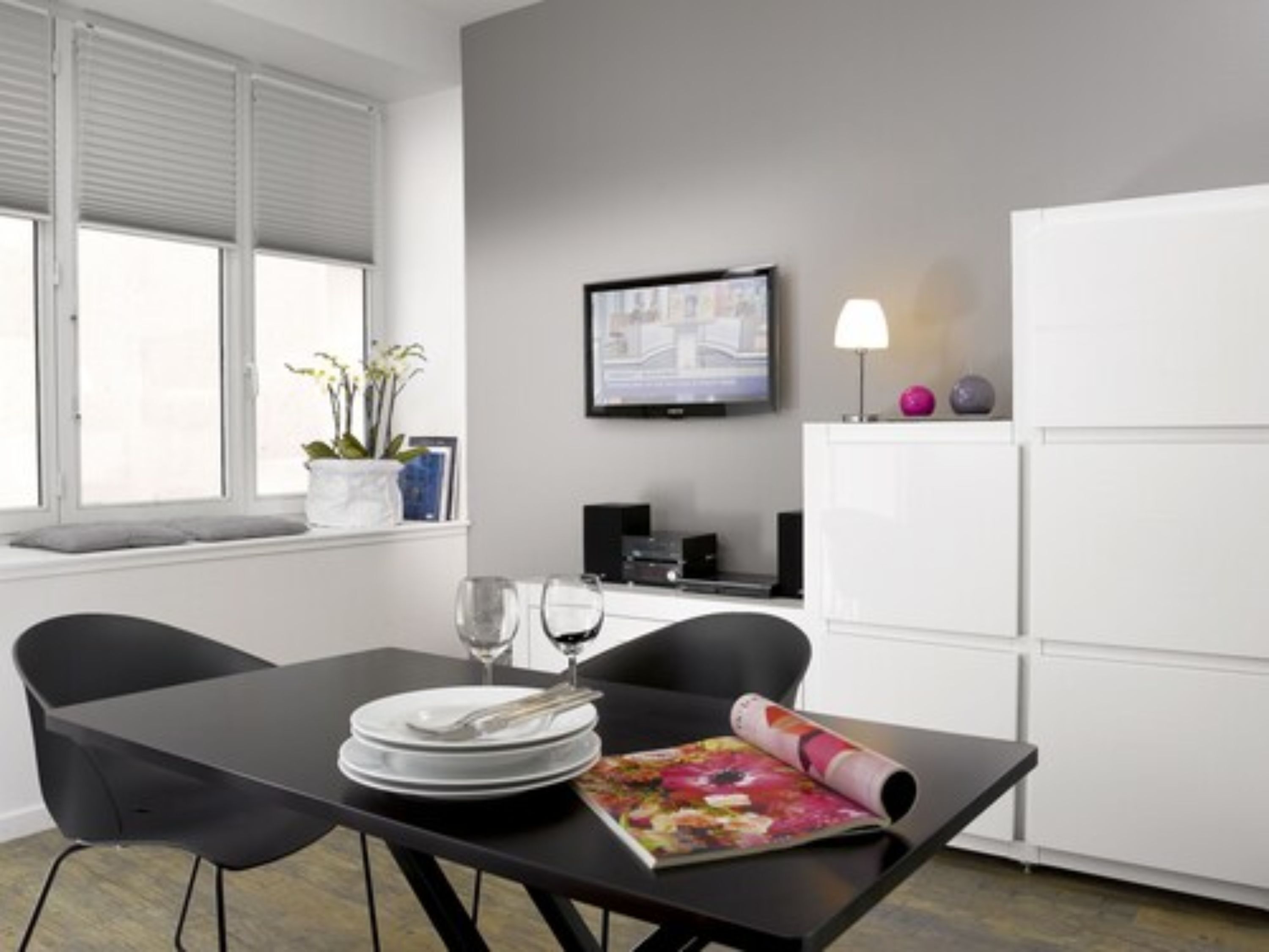 A modern room with a dining table, chairs, a TV, and a refrigerator.