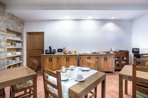 Une cuisine chaleureuse avec des meubles en bois, une table à manger pour quatre personnes et une étagère en pierre où sont disposés de la vaisselle.